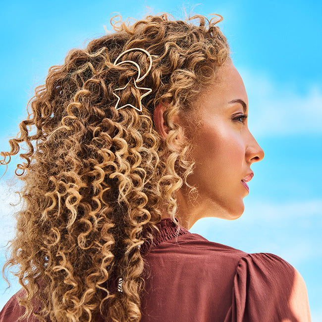 Woman with long, curly hair shown in profile wearing a gold Soulmates clip, against a blue sky