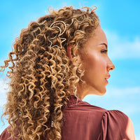 Woman with long, curly hair shown in profile wearing a gold Soulmates clip, against a blue sky