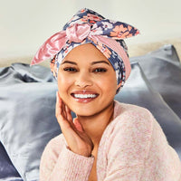 Smiling woman lying against pillows wearing the floral wrap cap tied in a bow on top of her head