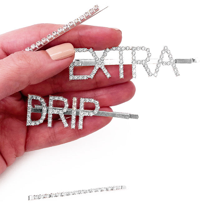 Hand holding rhinestone “Extra” and “Drip” barrettes, with a straight rhinestone barrette below
