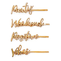 Four gold On The Go barrettes with the words “Party,” “Weekend,” “Positive,” and “Vibes” in script lettering
