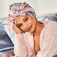 Woman holding the long ties of the floral wrap cap out to each side after placing it over her hair