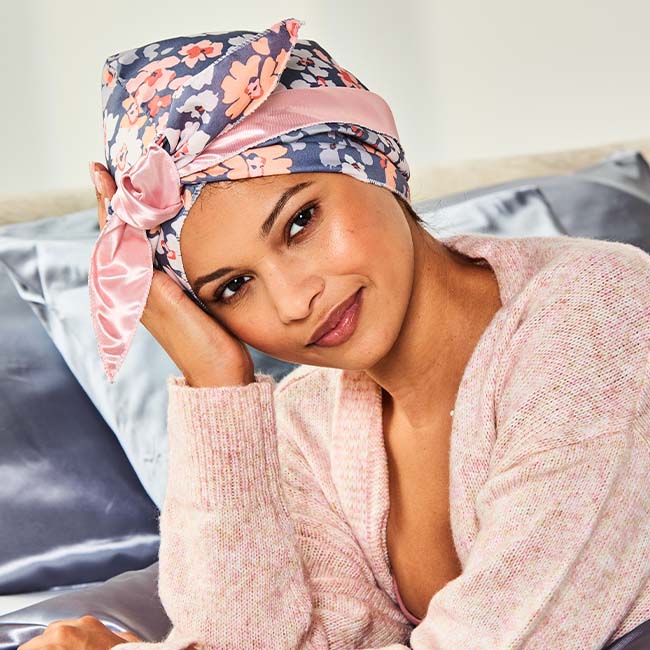 Woman holding the long ties of the floral wrap cap out to each side after placing it over her hair