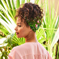 Back view of a woman wearing the tropical leaf print headband around her gathered curls, with palm leaves behind her