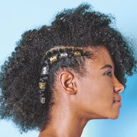 Woman with natural, curly hair shown in profile against a blue background, wearing metallic hair cuffs on small braids along the side of her head