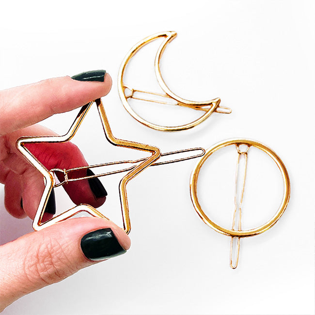 Hand with dark nail polish holding the gold star, moon, and circle Soulmates clips