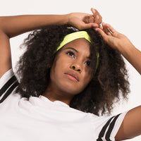 Woman with curly hair raising her arms, wearing the neon yellow Fitband headband at her hairline
