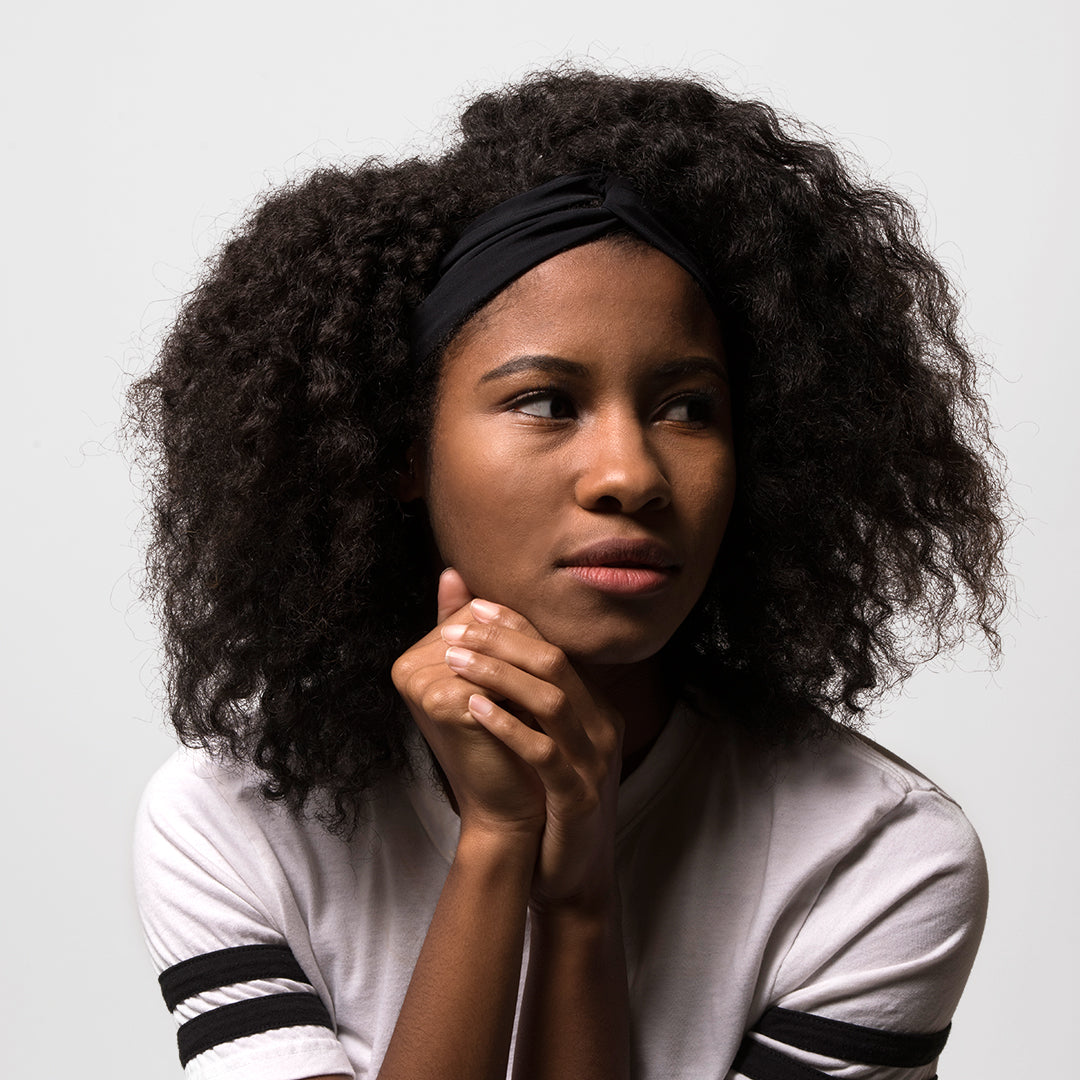 Woman with curly hair resting her chin on her hands, wearing the black Fitband headband