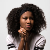 Woman with curly hair resting her chin on her hands, wearing the black Fitband headband