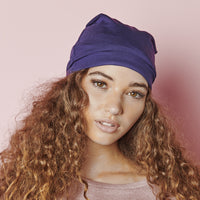 Woman with long, curly hair against a pink background, wearing the navy Satin-Lined Jersey Beanie